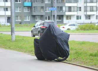 Motorcycle covered with a cover standing near the lawn, Yeremeyeva Street, Saint Petersburg, Russia, May 05, 2025