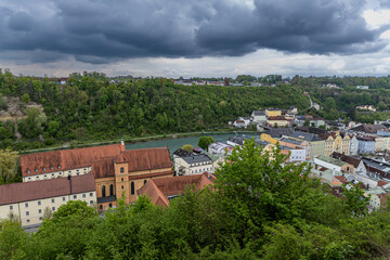 View from Burghausen Castle to the German town of Burghausen, the Salzach River, which is also the border with Austria, with a dramatic sky in the background and greenery in the foreground