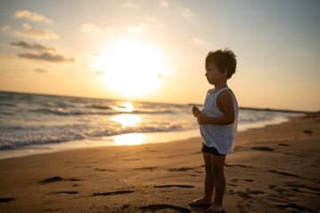 Little boy standing on beautiful beach with sunset.