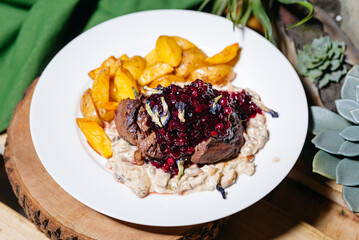 Seared Venison Steak with Berry Sauce and Potatoes. Rustic venison steak served with roasted golden potatoes, creamy mushroom sauce, and lingonberry topping, perfect for gourmet dining.