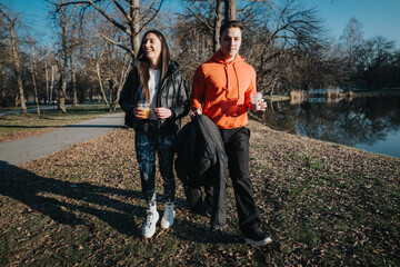 Two friends enjoying a casual stroll in a park on a sunny day, sipping beverages and sharing a...