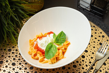Tagliatelle with tomato sauce and burrata. Fresh tagliatelle pasta served with creamy burrata cheese, tomato sauce, and basil leaves in a modern white bowl.