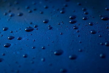 Close-up of water droplets on a dark surface with a blurred black background, creating a minimalistic and moody atmosphere.