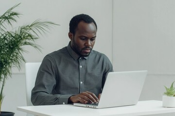 A focused African American man works diligently on his laptop, immersed in his task.