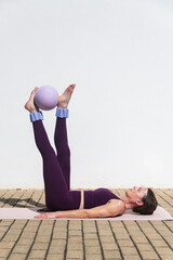 fit woman doing pilates exercises with a ball, legs raised
