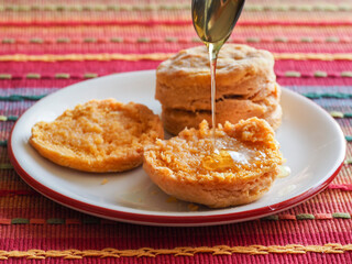 Close up of open sweet potato biscuit with honey dripping from a spoon, and an uncut one in the background