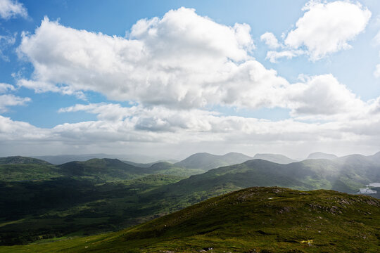 Lush green hills stretch across the landscape of Blackvalley, Ireland, showcasing the stunning natural beauty. The captivating clouds drift lazily in the bright sky, creating a serene atmosphere.