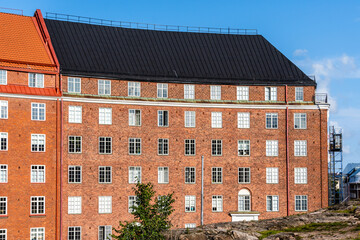 Vintage red brick buildings with colorful rooftops stand against a blue sky in Helsinki.