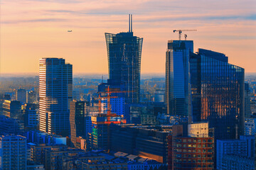 Dynamic sunset view of Warsaw modern skyline, with high-rise glass buildings and cranes symbolizing...