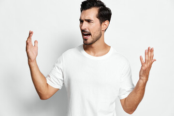 Expressive man gesturing with hands in frustration, wearing a casual white t-shirt, against a light...