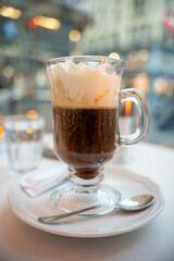 Close-up of a freshly served Viennese coffee with whipped cream in a clear glass mug, set on a white plate at a stylish European café. Perfect for food, travel, and holiday lifestyle visuals