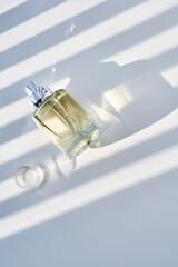 A bottle of perfume on a white background with stripes of shadows.
