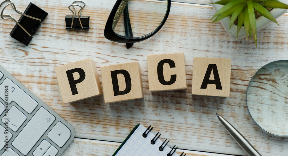 Poster the wooden block has the letters pdca on it. it is placed on a desk with a keyboard, a pen