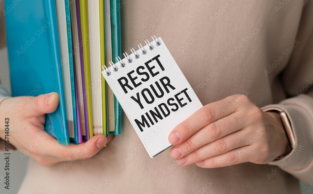 Poster a person holding a stack of books and a notebook with the words reset your mindset written on it