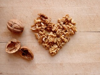 Top view of some shelled walnuts arranged in the shape of a heart on a wooden cutting board with a few empty nutshells and an unpeeled walnut.