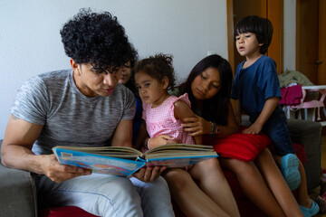 Hispanic family reading a book together on sofa at home