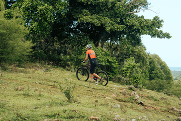 A cyclist pushes their mountain bike along a grassy path surrounded by vibrant foliage near ocean. 