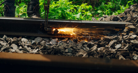 A worker in the process of arailroad track weld repair with a freight train passing