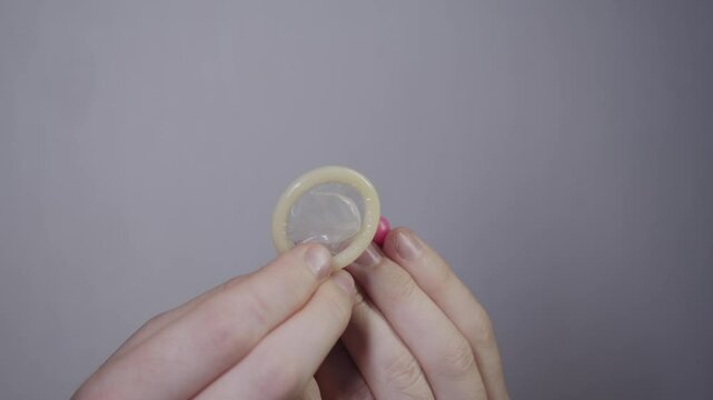Close-up of hands with pink birth control pill and condom. choosing most effective method of contraception to prevent unwanted pregnancy during sexual intercourse.