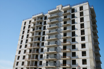 large grey brick multi-storey building under construction against a clear blue sky