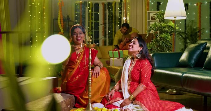 Lighting traditional samai with diya, Indian young girl in ethnic wear and senior mother joyfully celebrating Hindu festival Diwali in evening at home with festive decor and glowing diya illumination