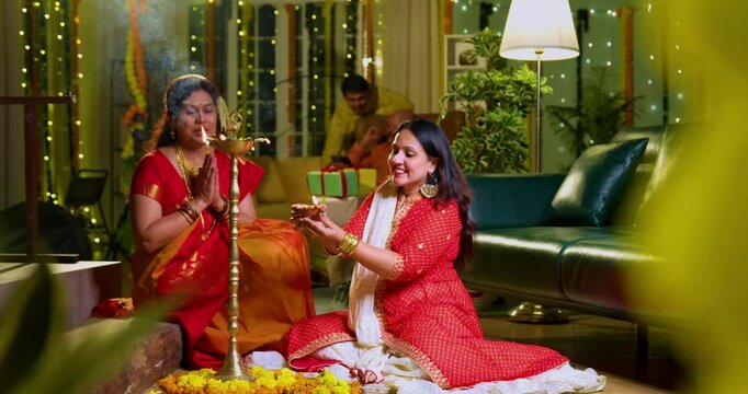 Lighting traditional samai with diya, Indian young girl in ethnic wear and senior mother joyfully celebrating Hindu festival Diwali in evening at home with festive decor and glowing diya illumination