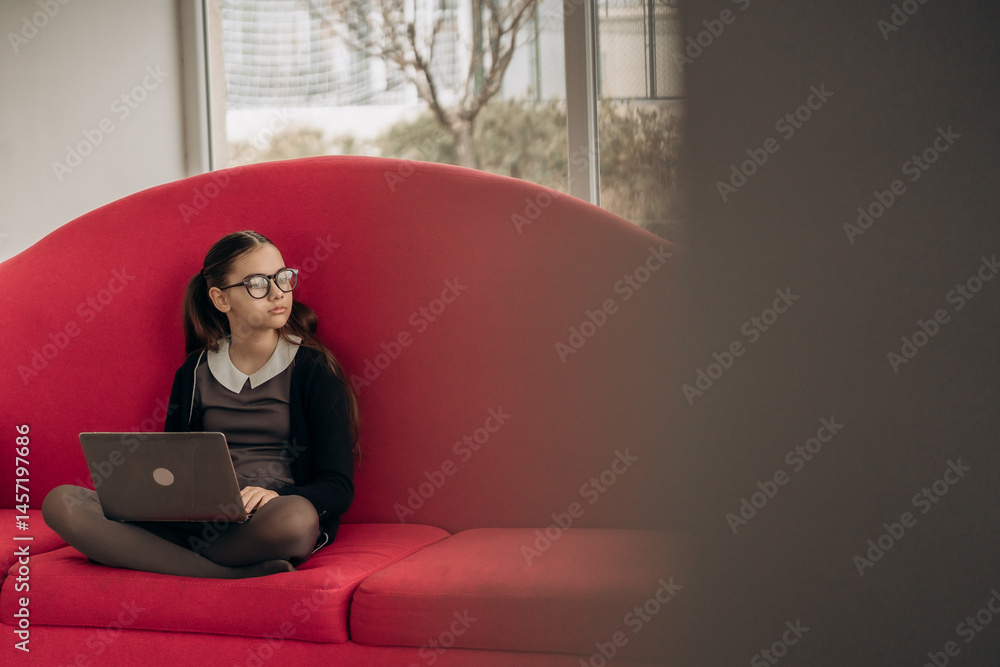 Poster young girl sitting with laptop on red sofa looking out window while studying at home showing moment 