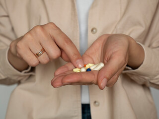 A young woman choosing a pill with her index finger, holding colorful pills in her hand. Concept of health, medication, pain relief, and self-care.