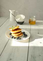 Cottage cheese pancakes with blueberries and sour cream on a white wooden table