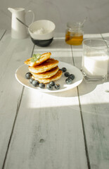 Cottage cheese pancakes with blueberries and sour cream on a white wooden table