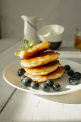 Cottage cheese pancakes with blueberries and sour cream on a white wooden table