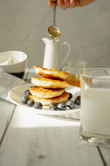 Cottage cheese pancakes with blueberries and sour cream on a white wooden table