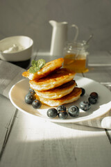 Cottage cheese pancakes with blueberries and sour cream on a white wooden table