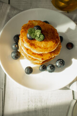 Cottage cheese pancakes with blueberries and sour cream on a white wooden table