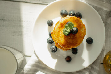 Cottage cheese pancakes with blueberries and sour cream on a white wooden table