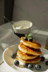Cottage cheese pancakes with blueberries and sour cream on a white wooden table