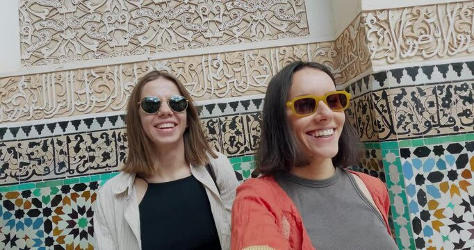 Happy smiling friends exploring Moroccan architecture in a traditional decorative site Madrasa Ben Youssef in Marrakesh, Morocco