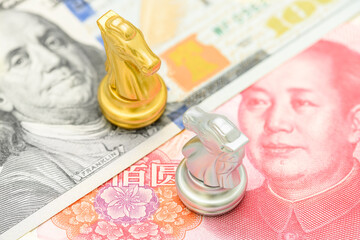 Trade war, reciprocal tariffs and global economic competition : Chess knight pieces on top of U.S. dollar and Chinese yuan notes, symbolizing the strategic economic rivalry between the US and China.