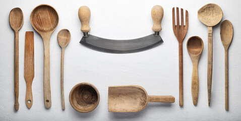 Mezzaluna knife, ladles and other old wooden kitchen tools on white plaster background, top view, space for text.