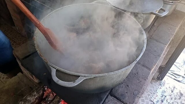 Traditional Brazilian Galinhada Cooked Over Wood Fire at Family Gathering. Stirring the chicken and seasonings.