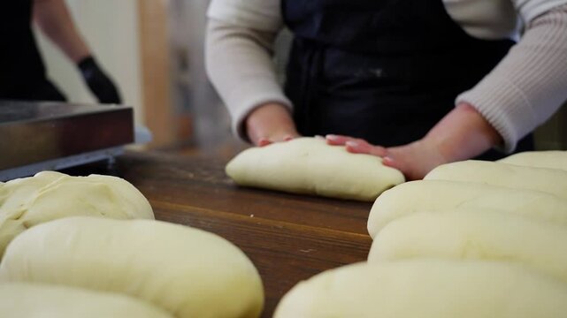 Baker hands skillfully kneading and forming bread loaves close-up of artisan bread preparation, fresh dough shaping in a professional bakery. High quality 4k footage