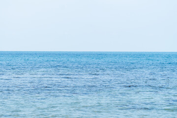 Expansive horizon where blue waves gently meet the tranquil waters under a clear sky