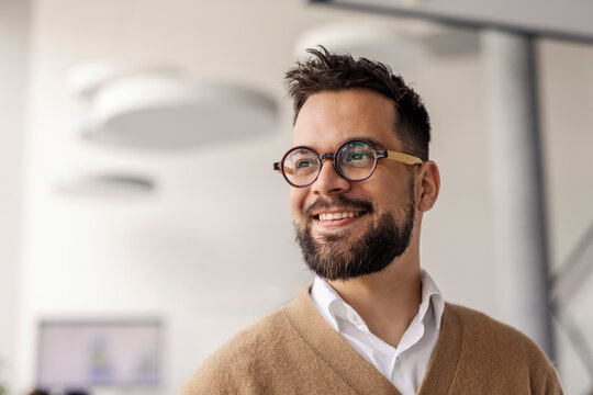 Headshot of a prospective innovative businessman smiling and looking away at corporate firm.