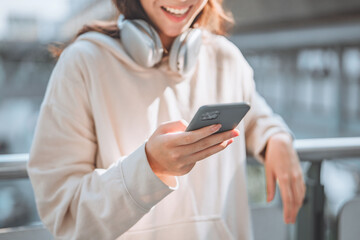 Fototapeta premium Close-up of happy asian teenage girl wearing headphones using smartphone in urban city – enjoying social media, online communication and digital lifestyle concept