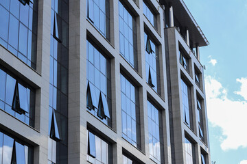 Glass windows of a modern office building in Minsk reflecting clouds and blue sky. A sleek, minimal look highlighting light, glass, and urban architecture.
