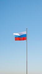 Large flag of the Russian Federation on a flagpole against a blue sky. Close up