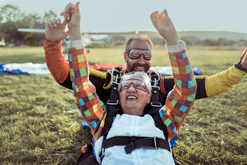 Happy senior woman celebrating after tandem skydive landing on grass field