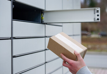 Hand placing or retrieving cardboard box from parcel locker. Close-up of a hand with cardboard box...