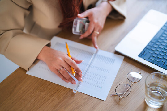 An Arab woman reviews financial documents at her desk. She uses a pencil and ruler to analyze the data, with a laptop and glasses nearby.