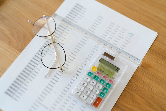 An Arab female is reviewing expenses. A calculator, ruler, and glasses rest on a document with financial data. budgeting and financial planning.